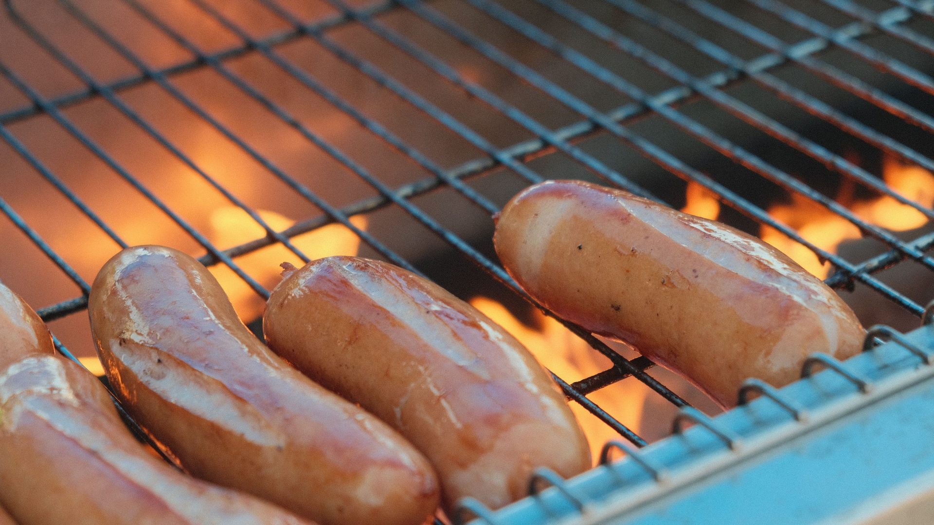 Rohe Bratwürste liegen über der offenen Grillflamme