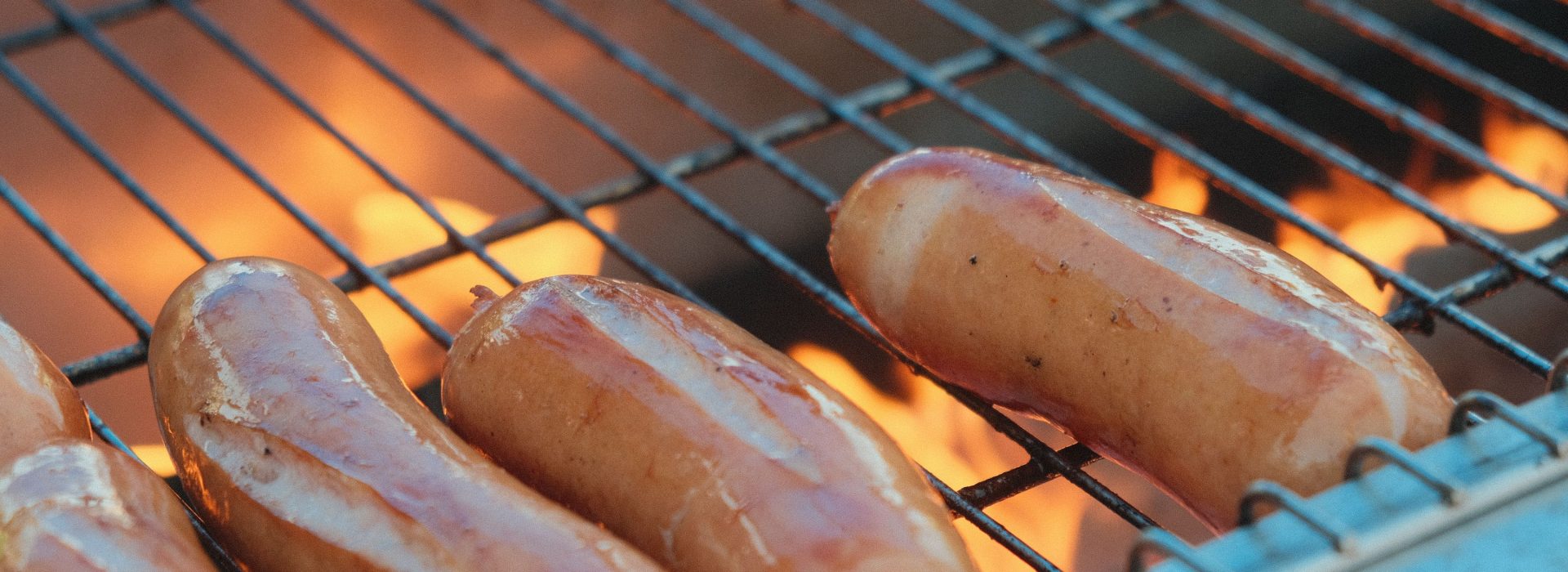 Rohe Bratwürste liegen über der offenen Grillflamme