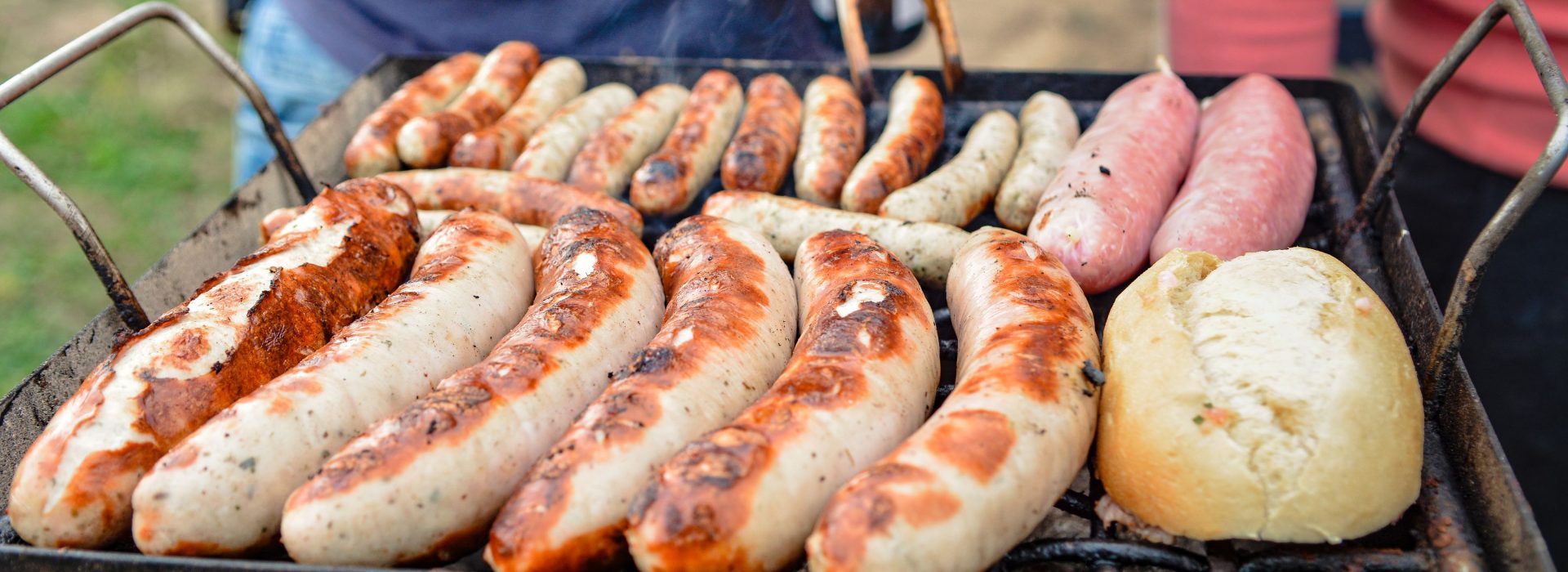 Person wendet Rostbratwürste mit der Grillzange auf dem Kohlegrill