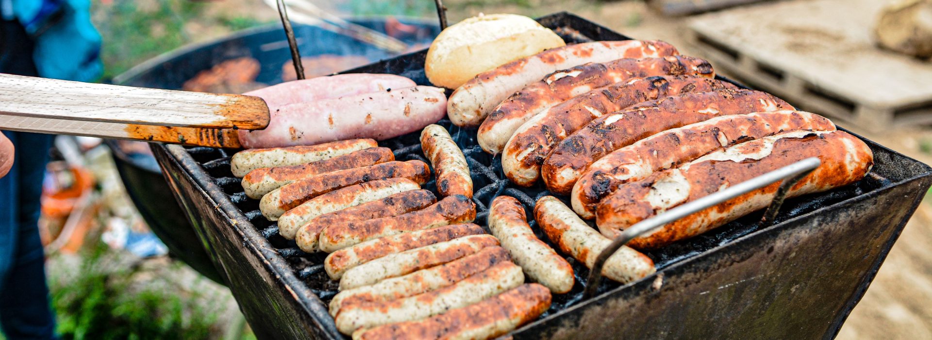 Nahaufnahme einer Hand, die Wurststücke auf dem Grill wendet